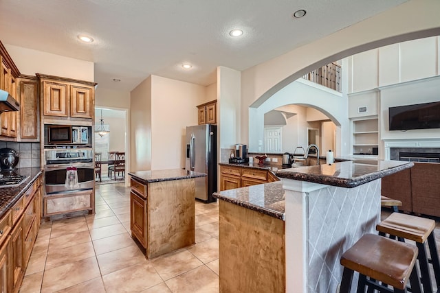 1102 Nautical Ln, Richmond, TX 77469 - kitchen with appliances with stainless steel finishes, a kitchen island, brown cabinets, dark stone counters, and a breakfast bar