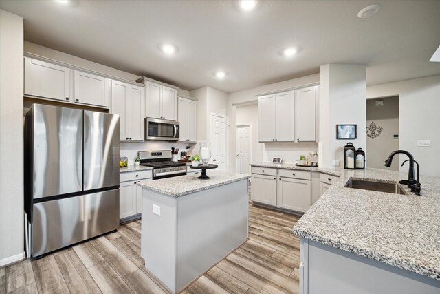 17218 Roxburgh Lake Ln, Hockley, TX 77447 - kitchen featuring appliances with stainless steel finishes, a sink, light stone countertops, light wood-style flooring, and recessed lighting