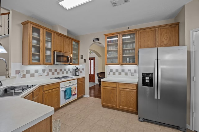 2615 Crystal Falls Dr, Pearland, TX 77584 - kitchen featuring stainless steel appliances, a sink, arched walkways, brown cabinetry, and backsplash