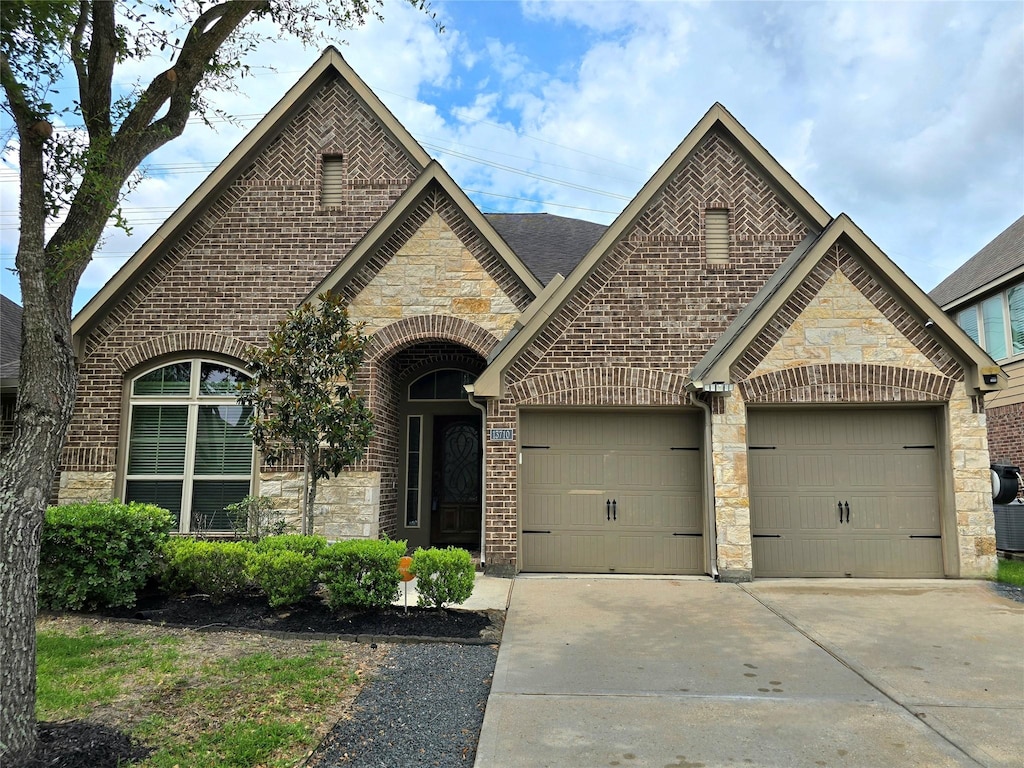 13710 Mooring Pointe Dr, Pearland, TX 77584 - french country inspired facade with stone siding, concrete driveway, a garage, brick siding, and roof with shingles