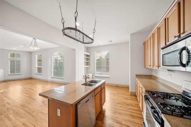 5012 Schuler St, Houston, TX 77007 - kitchen featuring appliances with stainless steel finishes, a sink, brown cabinets, light wood-style floors, and a kitchen island with sink