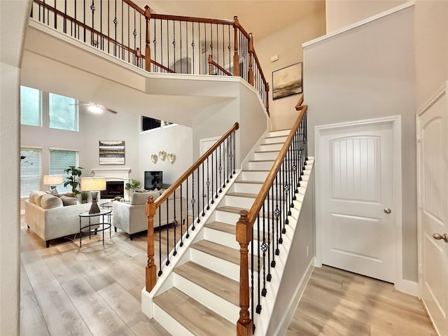 210 Black Swan Pl, The Woodlands, TX 77354 - staircase featuring a high ceiling, wood finished floors, a fireplace, a ceiling fan, and baseboards