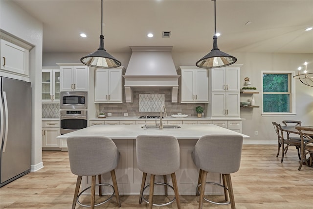 130 Playmoor Pl, Montgomery, TX 77316 - kitchen featuring appliances with stainless steel finishes, a sink, premium range hood, light countertops, and a breakfast bar