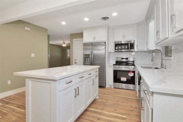 1105 W Dr, Port Neches, TX 77651 - kitchen featuring appliances with stainless steel finishes, a sink, white cabinetry, a kitchen island, and light wood finished floors