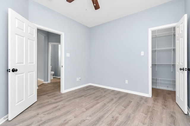 19 Long Springs Pl, The Woodlands, TX 77382 - unfurnished bedroom featuring a walk in closet, light wood-style floors, a closet, baseboards, and a ceiling fan