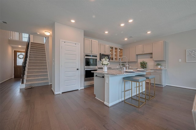 2923 Laurel Mill Way, Houston, TX 77080 - kitchen featuring stainless steel appliances, a center island with sink, tasteful backsplash, dark wood-style flooring, and glass insert cabinets