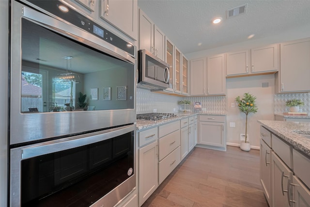 2923 Laurel Mill Way, Houston, TX 77080 - kitchen featuring stainless steel appliances, glass insert cabinets, decorative backsplash, light stone counters, and light wood-style flooring