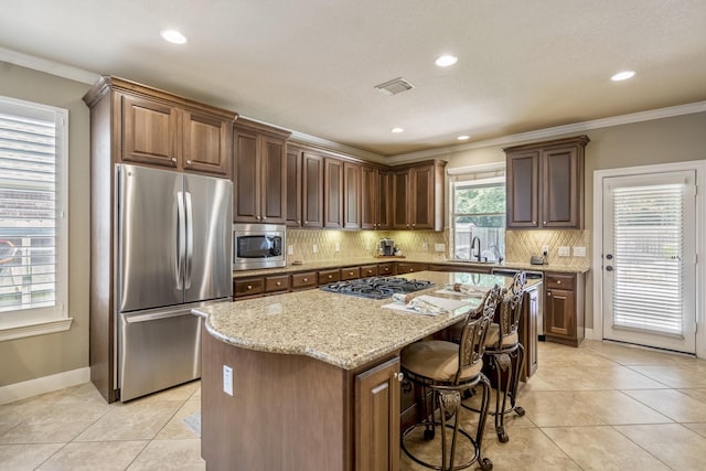 4611 Kings Landing Ln, Katy, TX 77494 - kitchen featuring appliances with stainless steel finishes, a center island, light stone countertops, tasteful backsplash, and light tile patterned flooring