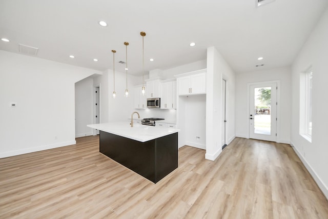 103 Frawley St, Houston, TX 77009 - kitchen featuring stainless steel appliances, white cabinetry, light wood finished floors, light countertops, and an island with sink