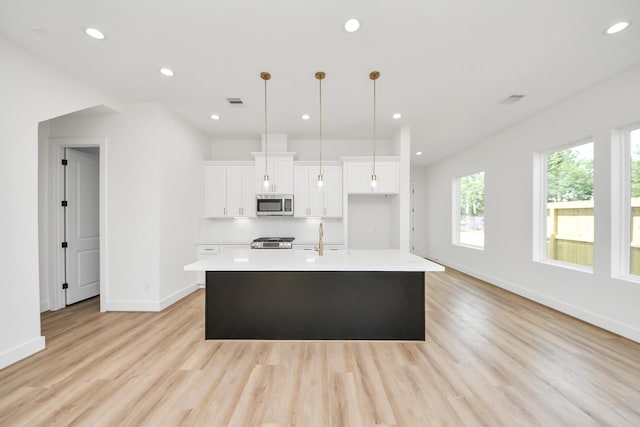 103 Frawley St, Houston, TX 77009 - kitchen with appliances with stainless steel finishes, a kitchen island with sink, light countertops, light wood-type flooring, and white cabinetry