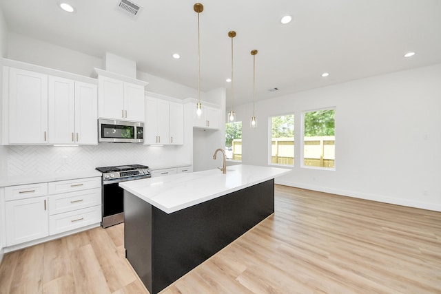 103 Frawley St, Houston, TX 77009 - kitchen featuring appliances with stainless steel finishes, a kitchen island with sink, tasteful backsplash, white cabinets, and light wood-type flooring