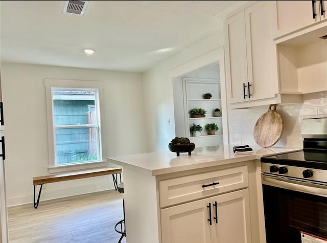319 Wisteria St, Lake Jackson, TX 77566 - kitchen with stainless steel electric range oven, white cabinetry, light wood-style floors, tasteful backsplash, and light countertops