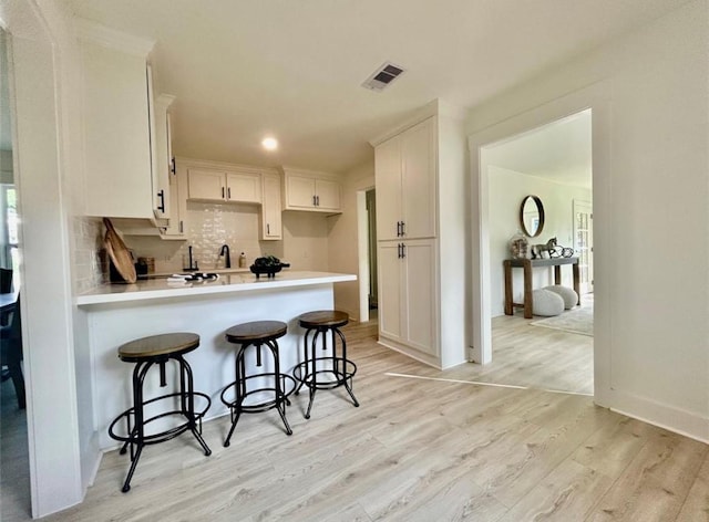 319 Wisteria St, Lake Jackson, TX 77566 - kitchen with light wood-style flooring, a peninsula, white cabinets, backsplash, and a kitchen bar