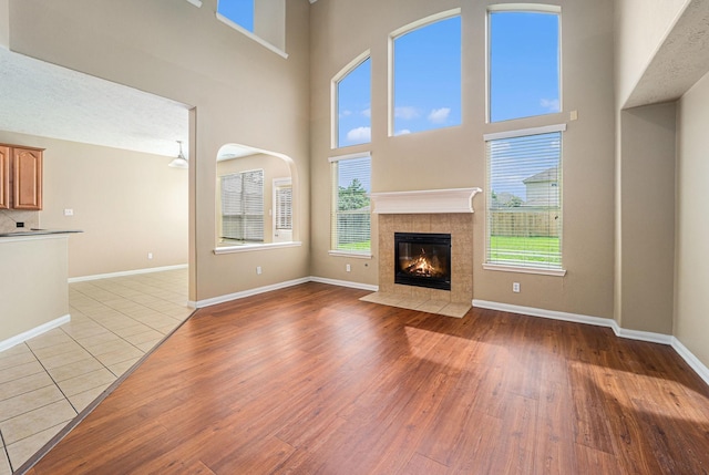 13707 Kingston River Ln, Houston, TX 77044 - unfurnished living room with light wood-style floors, a tile fireplace, baseboards, and a towering ceiling