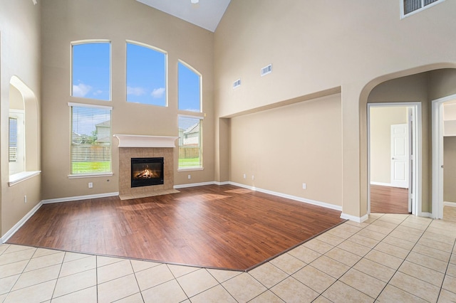 13707 Kingston River Ln, Houston, TX 77044 - unfurnished living room featuring light tile patterned floors, a high ceiling, a tile fireplace, arched walkways, and baseboards