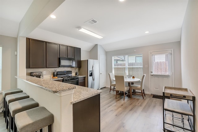 23607 Buttress Root Dr, Spring, TX 77373 - kitchen featuring black appliances, dark brown cabinets, a kitchen bar, lofted ceiling, and light wood-type flooring