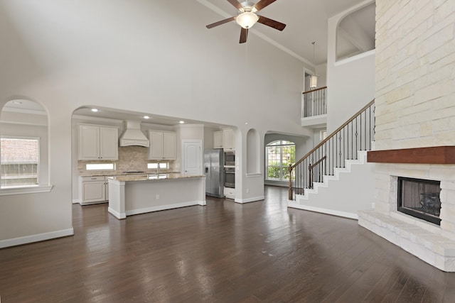 2131 Cranbrook Ridge Ln, Sugar Land, TX 77479 - unfurnished living room featuring ceiling fan, a fireplace, a towering ceiling, dark wood finished floors, and arched walkways