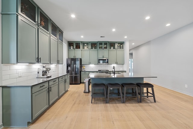 14027 Valley Creek Ct, Conroe, TX 77384 - kitchen featuring stainless steel appliances, a sink, decorative backsplash, light wood-type flooring, and a breakfast bar