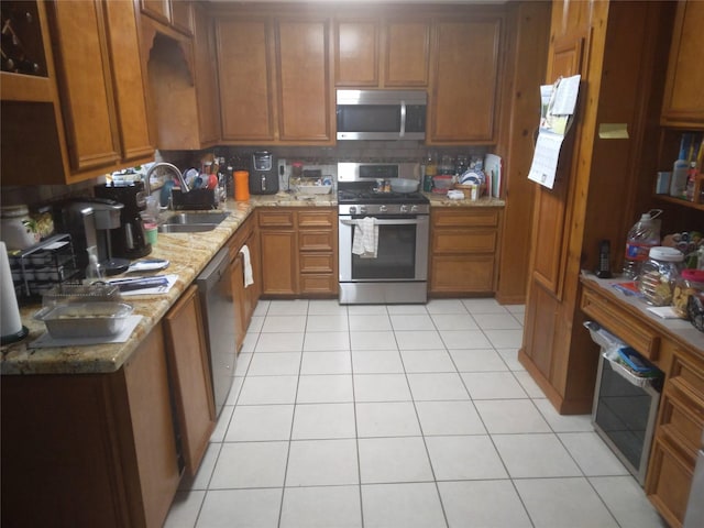 4802 Holly St, Bellaire, TX 77401 - kitchen featuring appliances with stainless steel finishes, brown cabinetry, a sink, light tile patterned floors, and light stone countertops