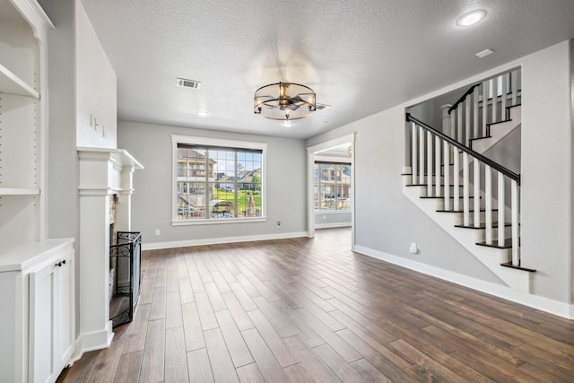 12336 Pebble View Dr, Conroe, TX 77304 - unfurnished living room featuring a textured ceiling, a chandelier, dark wood-style floors, a fireplace, and stairway