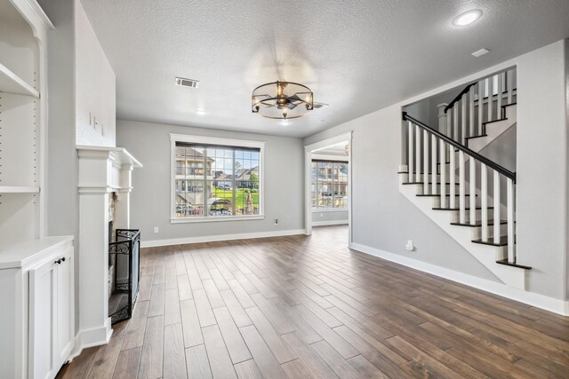 12336 Pebble View Dr, Conroe, TX 77304 - unfurnished living room with a textured ceiling, a chandelier, a fireplace, dark wood-style floors, and stairs