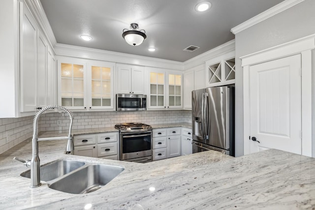 12336 Pebble View Dr, Conroe, TX 77304 - kitchen featuring appliances with stainless steel finishes, a sink, white cabinetry, decorative backsplash, and crown molding