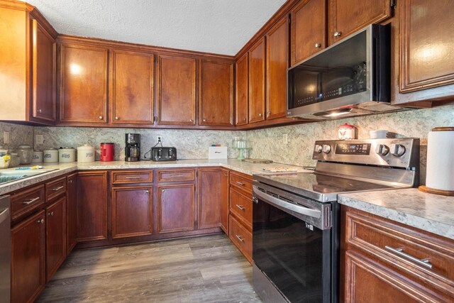 24027 Spears Cir, New Caney, TX 77357 - kitchen featuring stainless steel appliances, light wood finished floors, tasteful backsplash, light countertops, and a textured ceiling