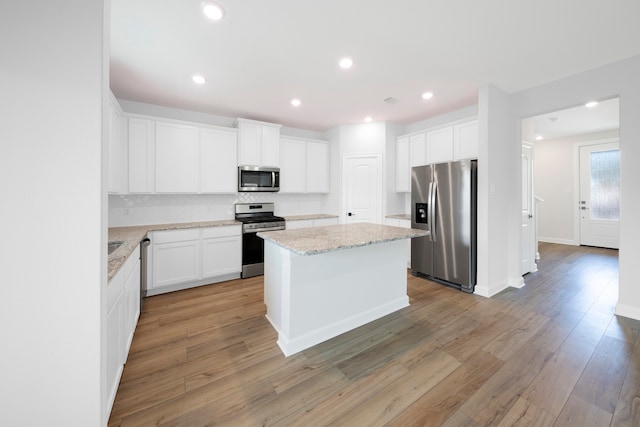 6179 White Spruce Dr, Conroe, TX 77304 - kitchen featuring appliances with stainless steel finishes, a center island, decorative backsplash, light wood-type flooring, and white cabinetry