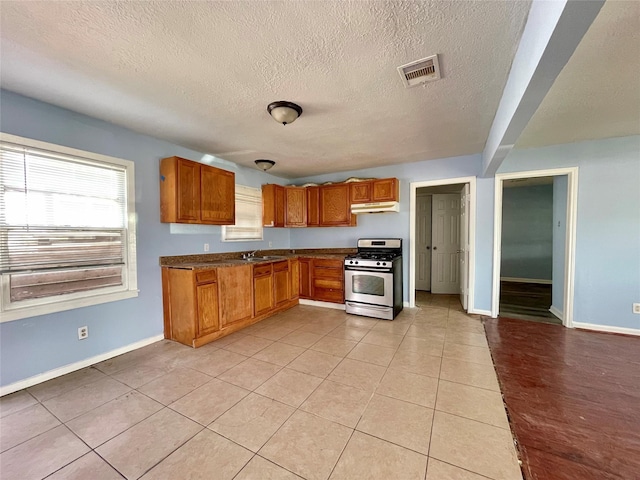 3707 Rosemont St, Houston, TX 77051 - kitchen with gas range, under cabinet range hood, brown cabinetry, baseboards, and a textured ceiling