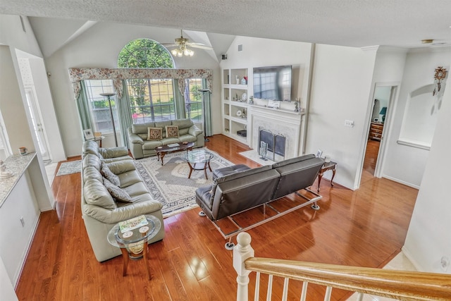 23207 Greenrush Dr, Katy, TX 77494 - living area featuring wood finished floors, a ceiling fan, a fireplace with flush hearth, vaulted ceiling, and a textured ceiling