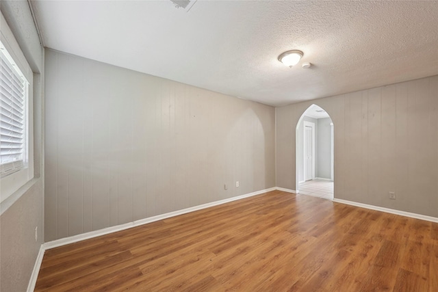 9270 Mclean St, Beaumont, TX 77707 - unfurnished room with light wood-style flooring, arched walkways, baseboards, a textured ceiling, and wood walls