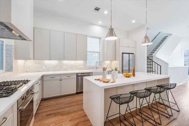 506 Parker St, Houston, TX 77007 - kitchen with wall chimney exhaust hood, stainless steel appliances, a kitchen bar, light wood-style flooring, and recessed lighting