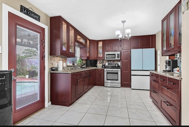 15133 Elstree Dr, Channelview, TX 77530 - kitchen featuring stainless steel appliances, a chandelier, light tile patterned floors, glass insert cabinets, and light stone counters