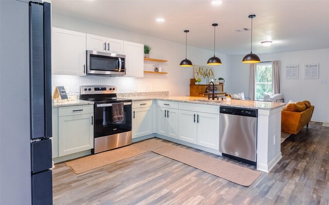 940 Cedar Point Dr, Livingston, TX 77351 - kitchen with appliances with stainless steel finishes, a peninsula, light wood finished floors, decorative backsplash, and open shelves