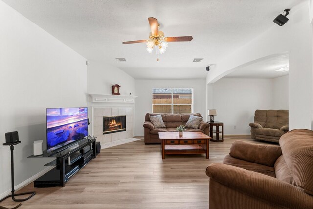 6107 Villa Hills Dr, Houston, TX 77066 - living room featuring light wood-style floors, a tiled fireplace, arched walkways, ceiling fan, and baseboards