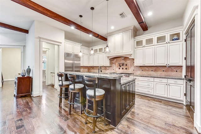 8305 Will Jordan Pkwy, Bellaire, TX 77401 - kitchen with stainless steel built in fridge, beam ceiling, a kitchen island with sink, tasteful backsplash, and light stone countertops