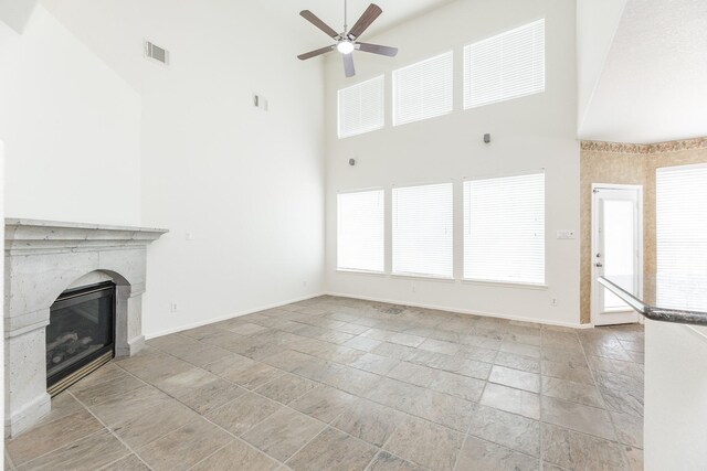 5923 Union Spgs, Sugar Land, TX 77479 - unfurnished living room with a towering ceiling, ceiling fan, a premium fireplace, baseboards, and light stone finish floors