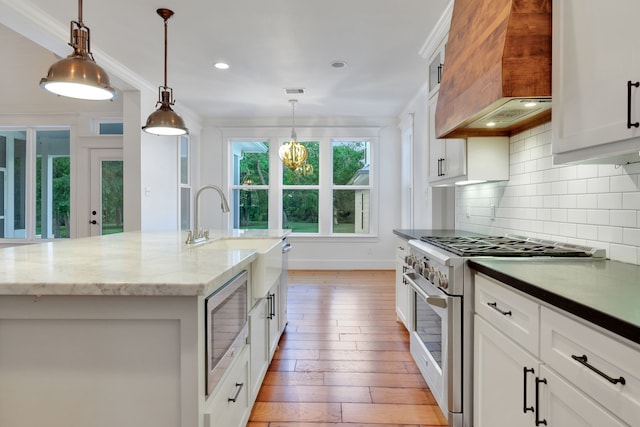 5926 Bit Pl, Baytown, TX 77523 - kitchen featuring stainless steel appliances, custom exhaust hood, light wood-style flooring, backsplash, and a chandelier
