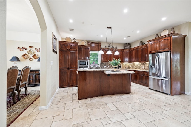 8917 Hawk Rd, Pearland, TX 77584 - kitchen featuring appliances with stainless steel finishes, a kitchen island, stone tile flooring, decorative backsplash, and arched walkways
