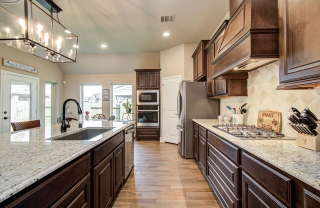 2335 Mayfield Trail Ct, League City, TX 77573 - kitchen with appliances with stainless steel finishes, a sink, custom exhaust hood, tasteful backsplash, and light wood finished floors