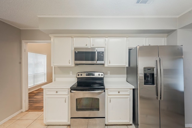 19523 Enchanted Grove Dr, Spring, TX 77388 - kitchen featuring appliances with stainless steel finishes, light countertops, light tile patterned flooring, white cabinetry, and ornamental molding