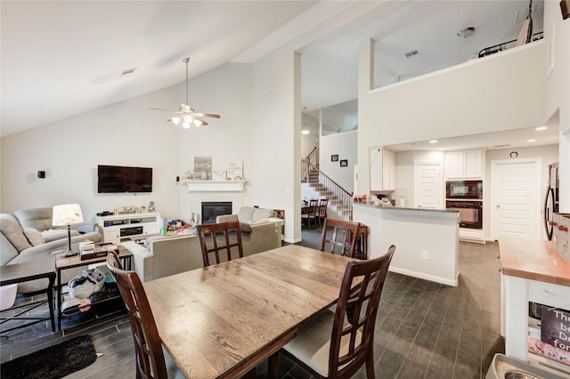 18226 Golden Falls Ln, Spring, TX 77379 - dining area with stairway, dark wood-style flooring, a glass covered fireplace, high vaulted ceiling, and ceiling fan