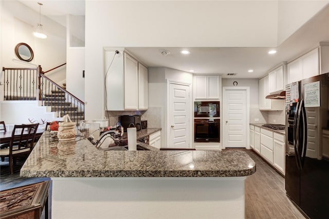 18226 Golden Falls Ln, Spring, TX 77379 - kitchen with black appliances, a towering ceiling, under cabinet range hood, a peninsula, and wood finished floors