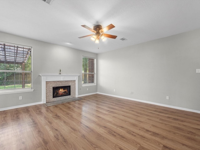 3910 Echo Mountain Dr, Kingwood, TX 77345 - unfurnished living room featuring plenty of natural light, a ceiling fan, a warm lit fireplace, and wood finished floors