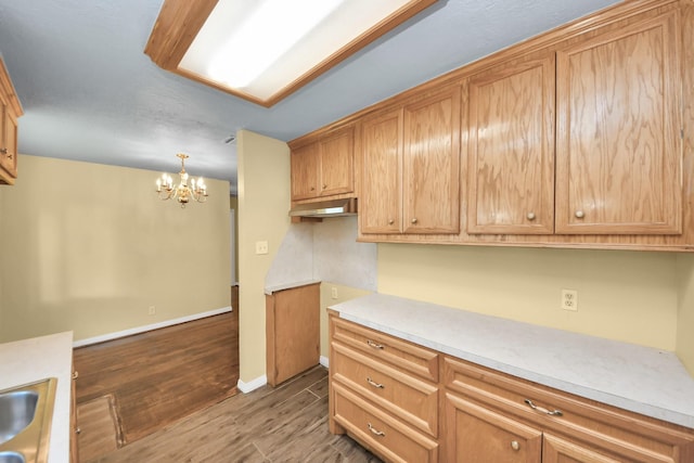149 E Riverwood Dr, Houston, TX 77076 - kitchen with wood finished floors, a chandelier, light countertops, baseboards, and under cabinet range hood