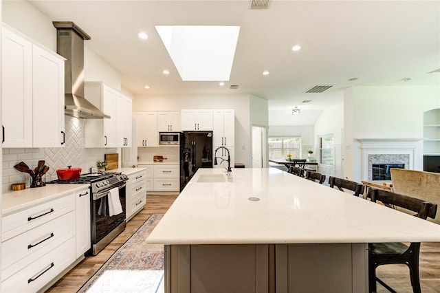 12006 Bright Landing Ct, Pearland, TX 77584 - kitchen with stainless steel appliances, wall chimney exhaust hood, a breakfast bar area, a sink, and light wood-style floors