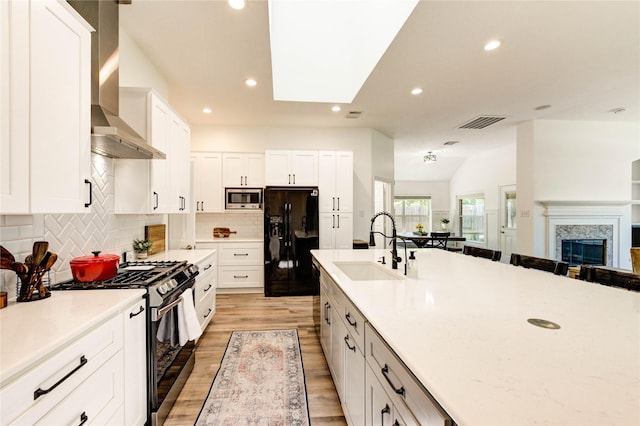 12006 Bright Landing Ct, Pearland, TX 77584 - kitchen featuring appliances with stainless steel finishes, wall chimney range hood, a sink, light wood-style floors, and recessed lighting
