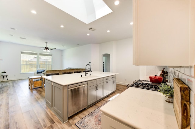 12006 Bright Landing Ct, Pearland, TX 77584 - kitchen featuring stainless steel dishwasher, a sink, arched walkways, open floor plan, and light wood-style floors