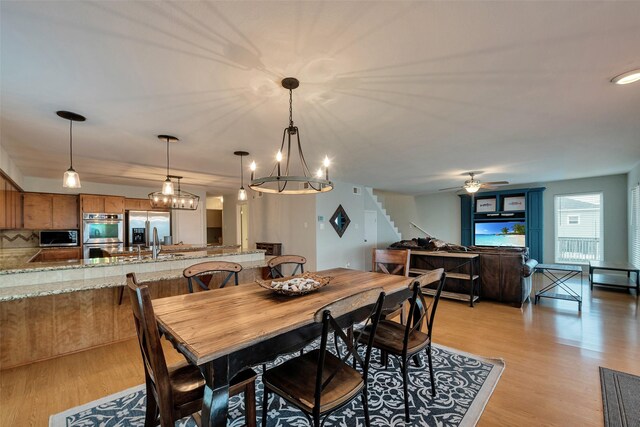 1327 Tiki Dr, Tiki Island, TX 77554 - dining space featuring light wood-type flooring, stairway, a chandelier, and a ceiling fan