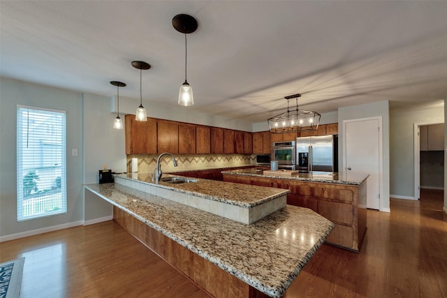 1327 Tiki Dr, Tiki Island, TX 77554 - kitchen featuring stainless steel appliances, a sink, brown cabinets, baseboards, and a peninsula